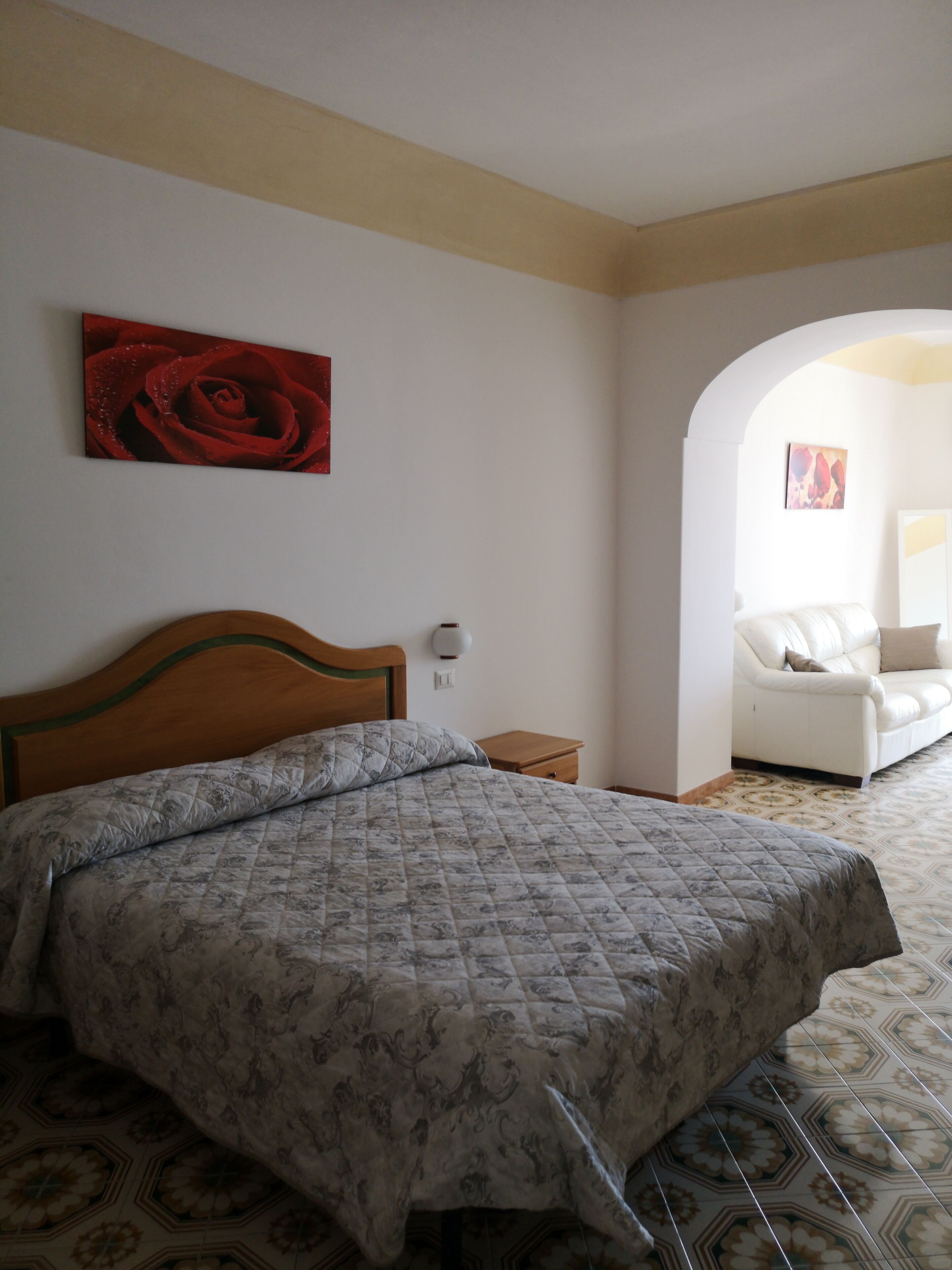 Um quarto com cama, mesa de cabeceira, sofá branco e um quadro na parede.