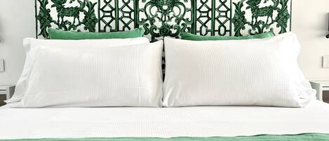 Una cama con sábanas blancas, un plaid verde y un cabecero decorativo con un estampado geométrico.