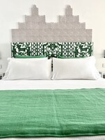 Una cama con sábanas blancas, un plaid verde y un cabecero decorativo con un estampado geométrico.