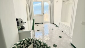 Una camera d'albergo con un divano verde, vista mare attraverso un'ampia finestra e pavimento piastrellato.