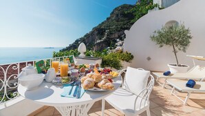 Una terrazza con tavolo apparecchiato per la colazione, con vista sul paesaggio costiero.