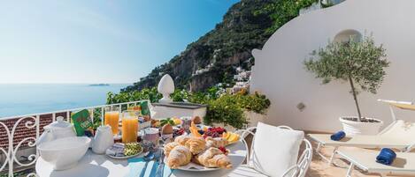 A terrace with a table set for breakfast, overlooking a coastal landscape.