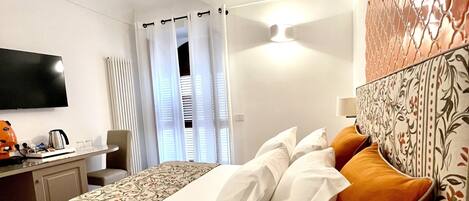 A modern hotel room with a large bed, a flat-screen TV, a desk with a kettle, and a decorative headboard.