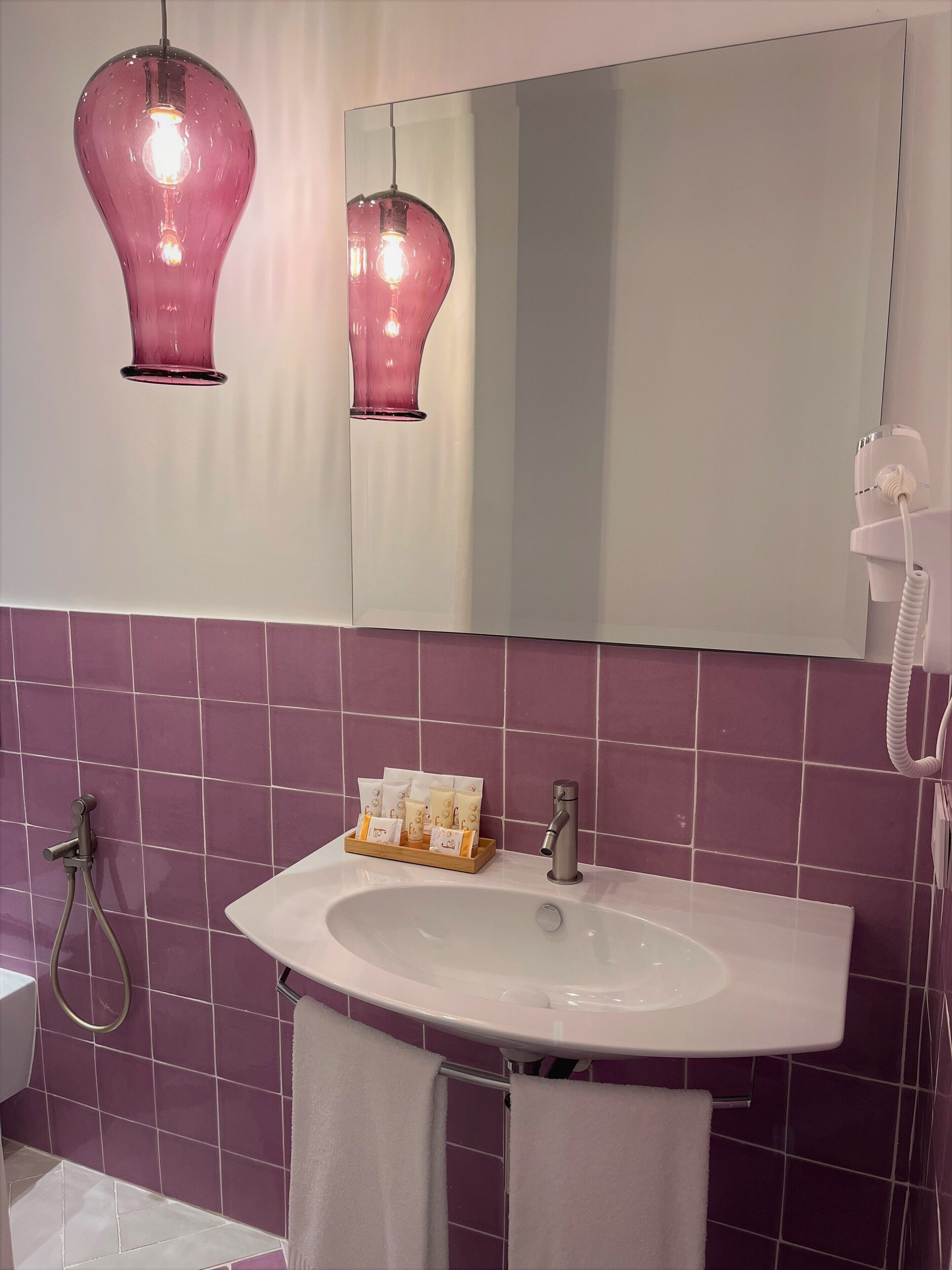 A bathroom with a white sink, purple tiles, a mirror, and two pendant lights.