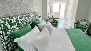 Una camera d'albergo moderna con un grande letto, una testiera a motivi verdi e bianchi e vista sulla zona esterna attraverso un arco.