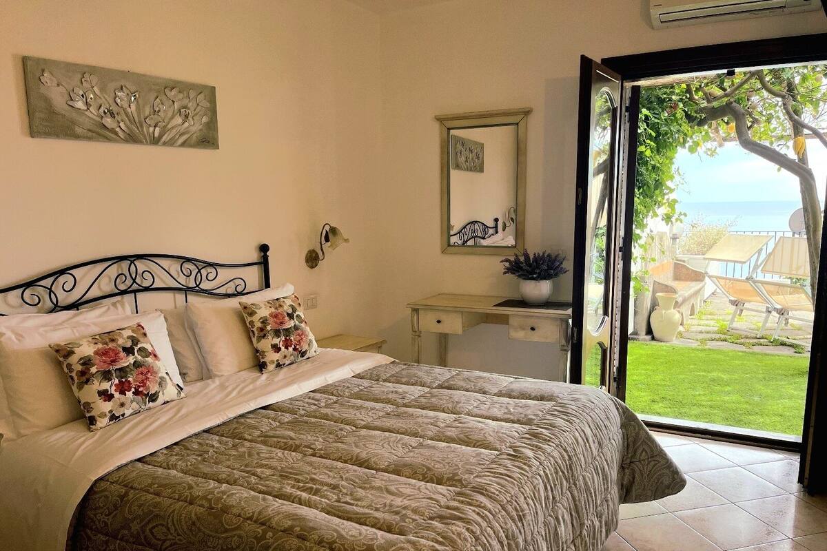 A bedroom with a bed, a desk, and a view of the outdoors.