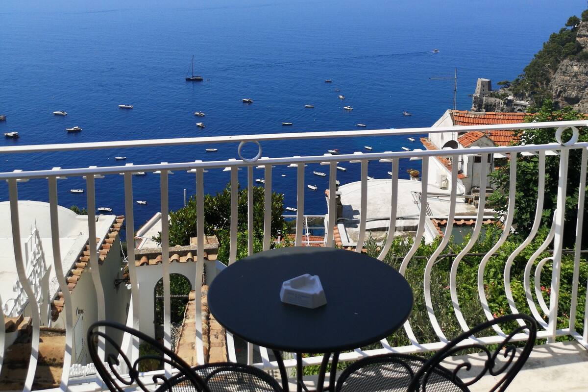 A balcony with a table and chairs overlooking a coastal view with boats.