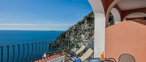 A balcony with a view of the sea, a table with chairs, and a drink.