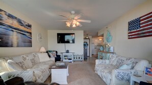 A living room with two sofas, a coffee table, a TV, and a ceiling fan. - Experience oceanfront living at Shipwatch Villas 1209 in North Topsail Beach! (North Topsail Beach)