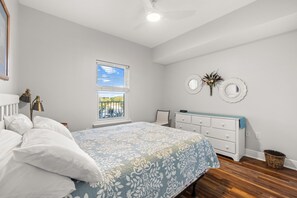 Un dormitorio con cama, cómoda, ventana y ventilador de techo.