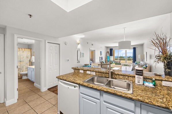 A modern kitchen with granite countertops, a dishwasher, and a view of the living area.