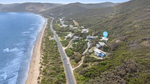 An aerial view of a coastal area with a road leading to a cluster of houses. - The Surf Spot - Absolute beach front (Eastern View)
