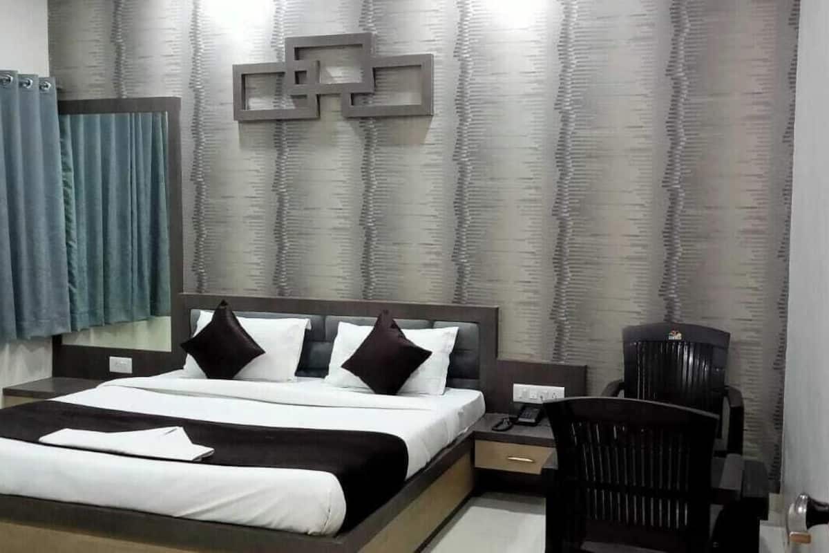 A modern hotel room with a large bed, a desk, a chair, and a wall-mounted TV.