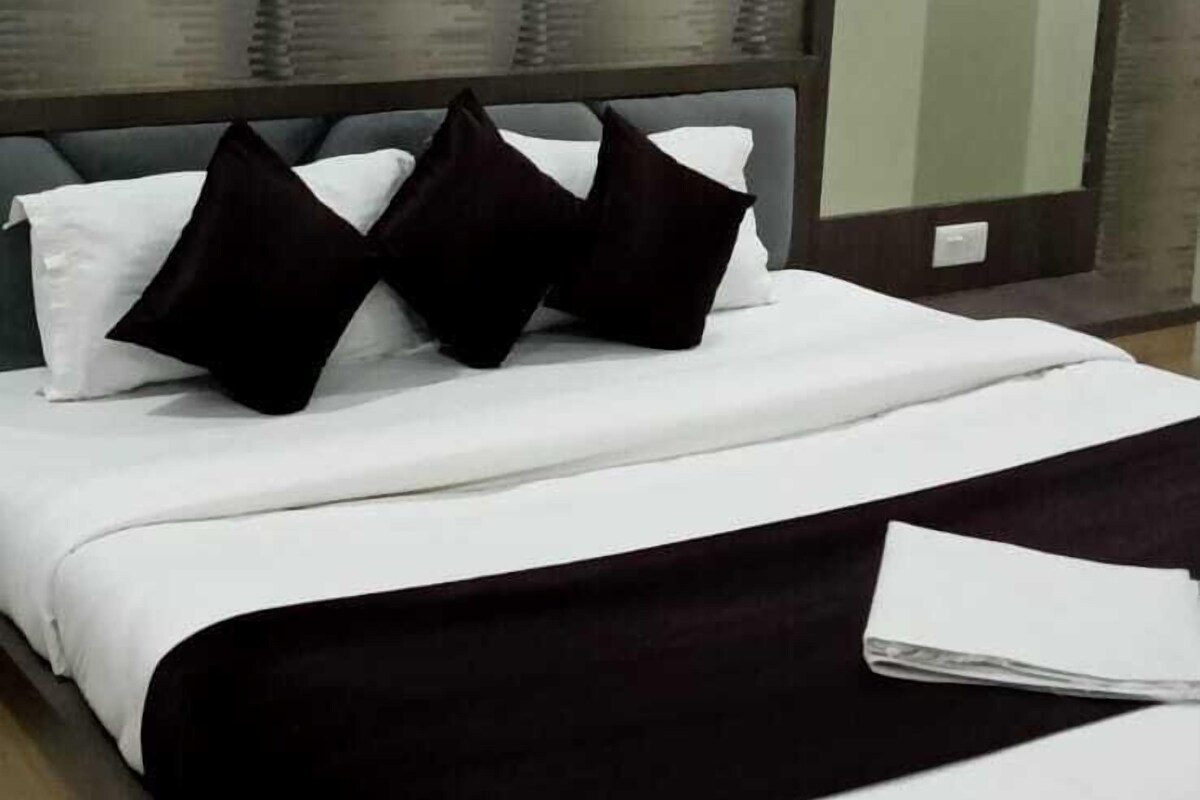 A neatly made bed with white and black bedding, a dark headboard, and a large mirror on the wall.