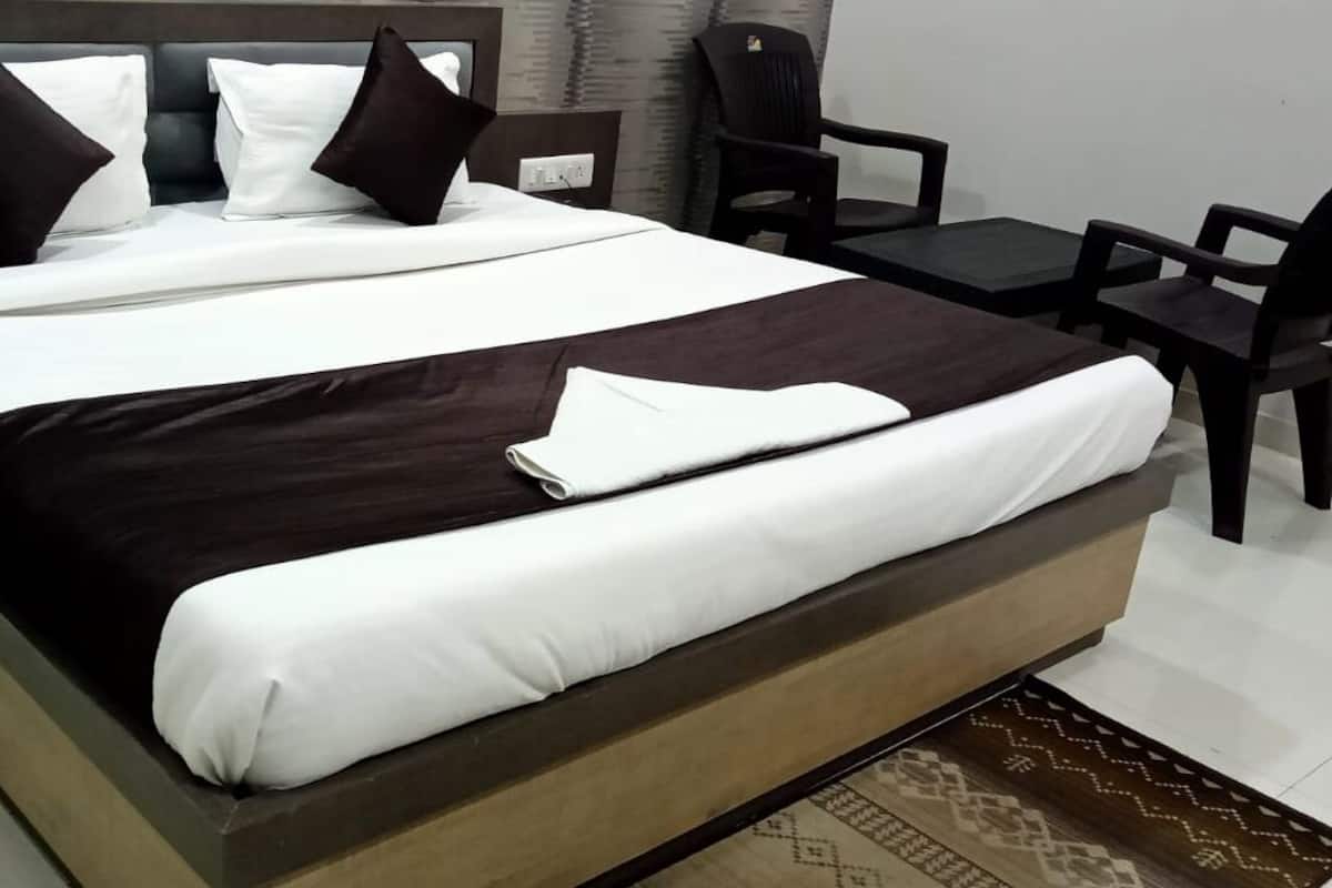 A neatly made bed with white and brown bedding, a small table with chairs, and a patterned rug.