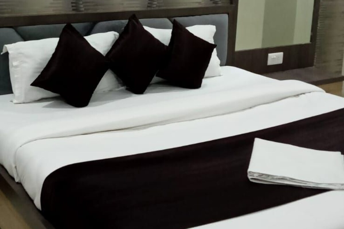 A neatly made bed with white and black bedding, a dark headboard, and a large mirror on the wall.