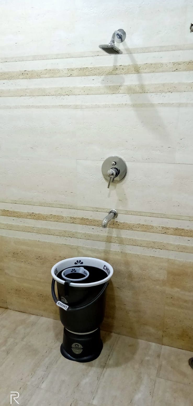 A bathroom with a shower, a toilet, and a bucket.
