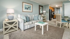 A living room with a striped sofa, a small white table, a lamp, and a framed picture on the wall. - Great Oceanfront 1 Bedroom in Desirable North Ocean City (Ocean City)