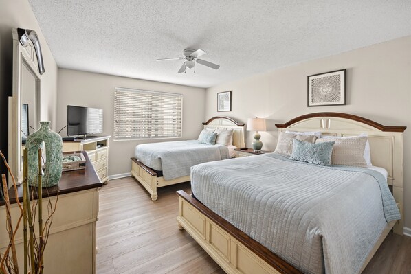 A bedroom with two beds, a ceiling fan, a TV, and a window with blinds. - Sky High Ocean View-Brighton 1202 2 Br Oceanfront (Myrtle Beach)