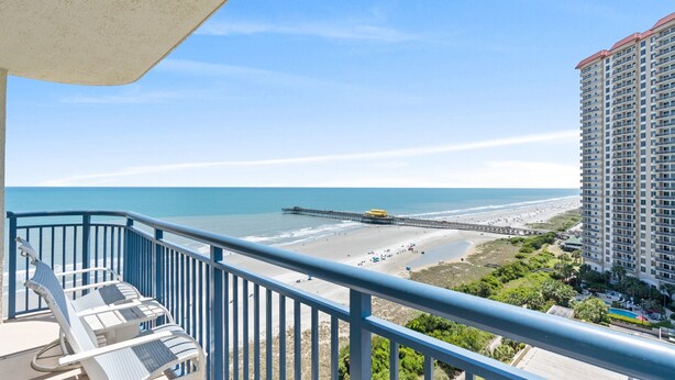 Een balkon met uitzicht op een strand, een pier en een hoog gebouw.