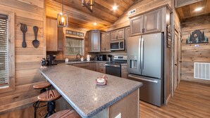 Een moderne keuken met houten wanden, granieten aanrechtbladen en roestvrijstalen apparatuur, plus barstoelen.