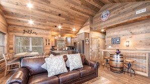 Een gezellig chaletinterieur met een bruine leren bank, een houten eettafel en een bar met krukken.