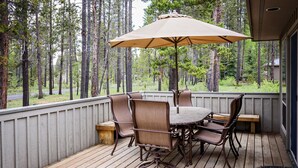 Un espace extérieur abrité, doté d’une table et de chaises, entouré d’une terrasse en bois et offrant une vue sur une forêt.