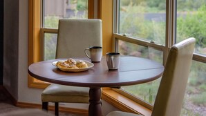 Une table à manger avec une assiette de nourriture et une tasse, placée près d’une fenêtre donnant sur un paysage verdoyant.