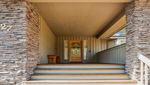 Un porche revêtu de pierres, avec une porte en bois et des marches menant à un vestibule abrité.