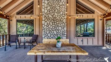 A wooden deck with a stone wall, two windows, and a table with chairs.