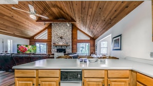 A spacious kitchen with wooden cabinets, a central island, and a stone fireplace. - Cobblestone Cottage | Dog-Friendly Escape w/ Stone Hearth & Pines (Ruidoso)