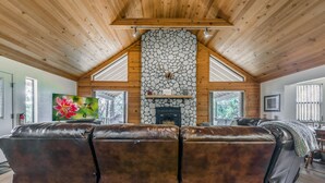 A cozy living room with a stone fireplace, leather sofas, and wooden ceiling beams. - Cobblestone Cottage | Dog-Friendly Escape w/ Stone Hearth & Pines (Ruidoso)