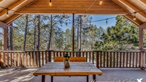 A wooden deck with a table and bench, surrounded by a wooden railing, overlooking a forested area. - Cobblestone Cottage | Dog-Friendly Escape w/ Stone Hearth & Pines (Ruidoso)
