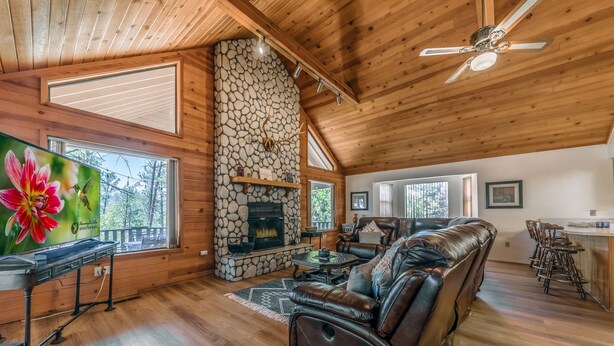 A cozy cabin interior with a stone fireplace, wooden ceiling, and a leather sofa. - Cobblestone Cottage | Dog-Friendly Escape w/ Stone Hearth & Pines (Ruidoso)