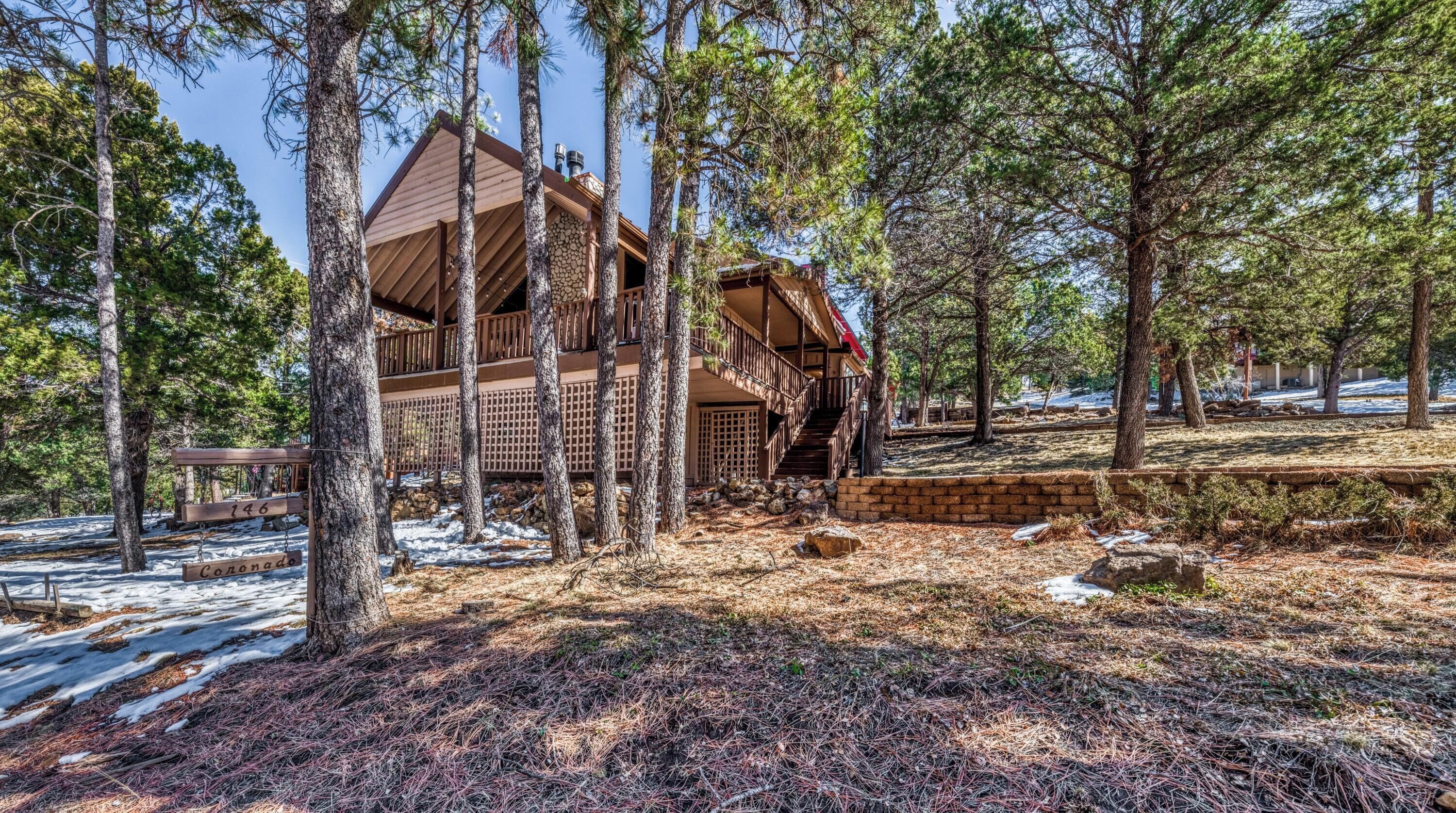 A cabin with a wooden exterior, surrounded by tall pine trees, and a stone wall in the foreground.