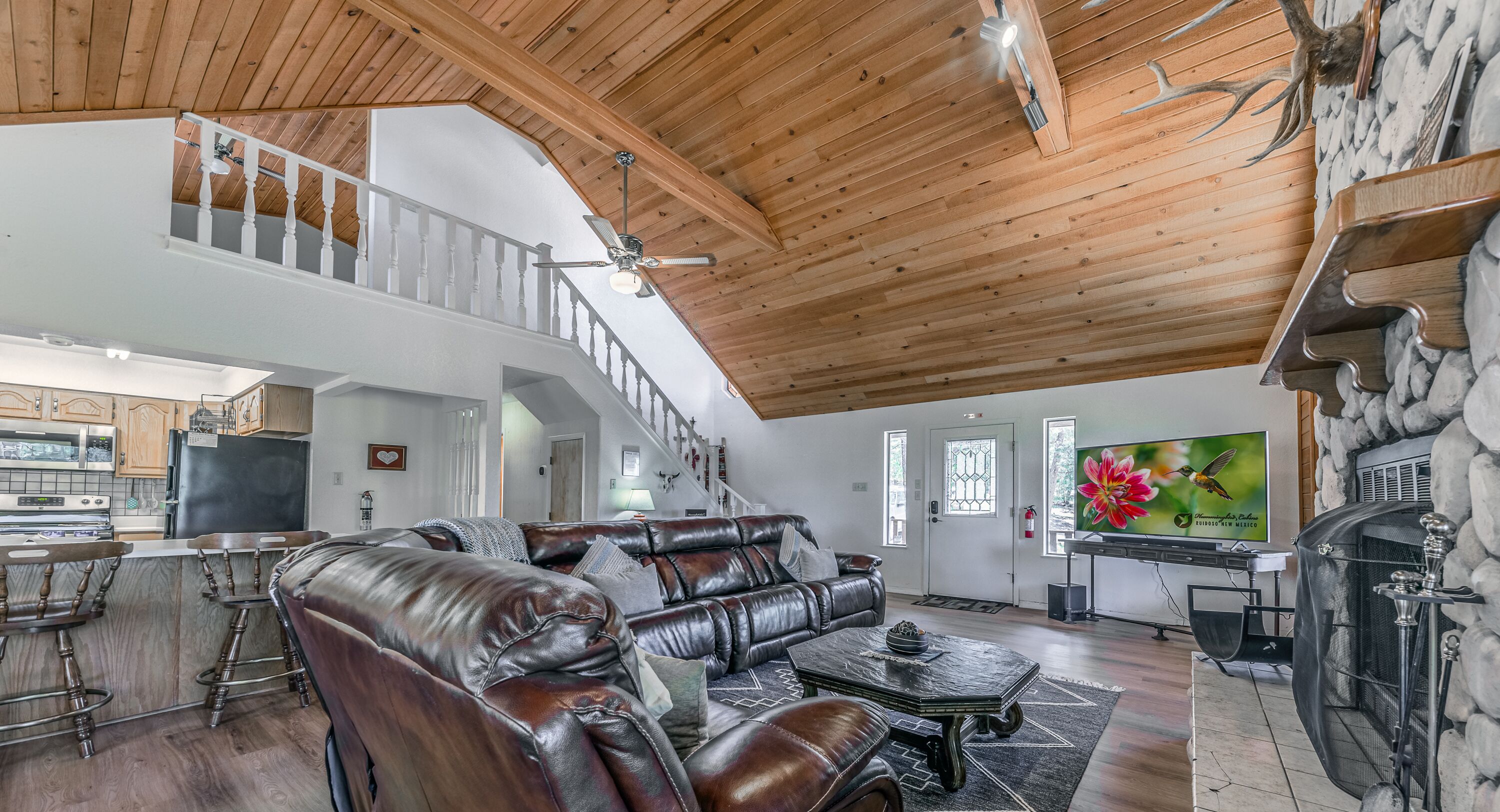 A spacious living room with a high ceiling, leather sofas, a dining area with bar stools, and a stone fireplace.