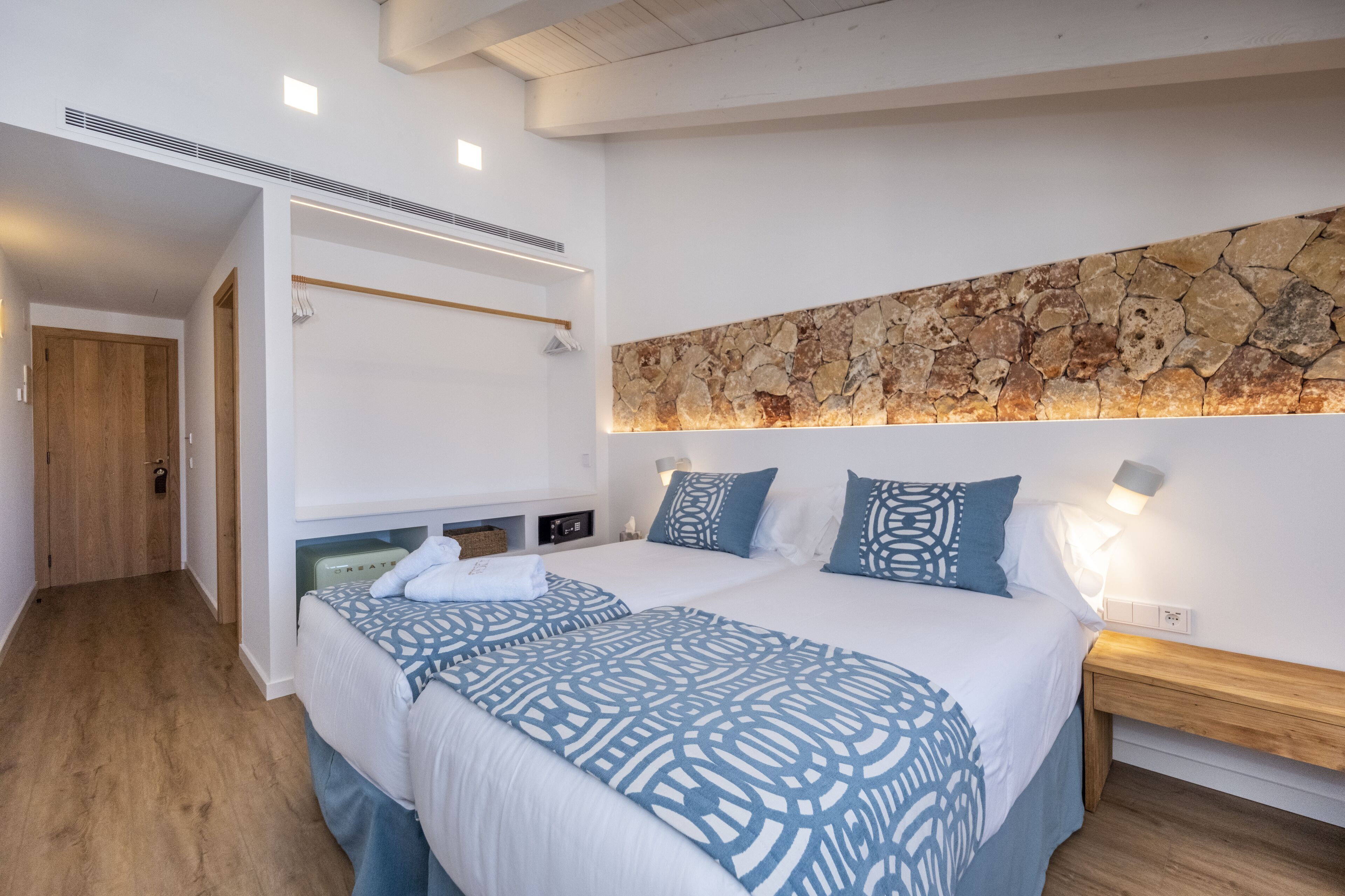 A modern hotel room with a large bed, a stone accent wall, and a wooden floor.