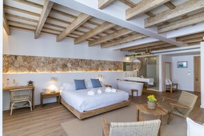 Un dormitorio moderno con pared de piedra, vigas de madera en el techo, una cama grande, mesitas de noche, un escritorio y una zona de estar con muebles de mimbre.