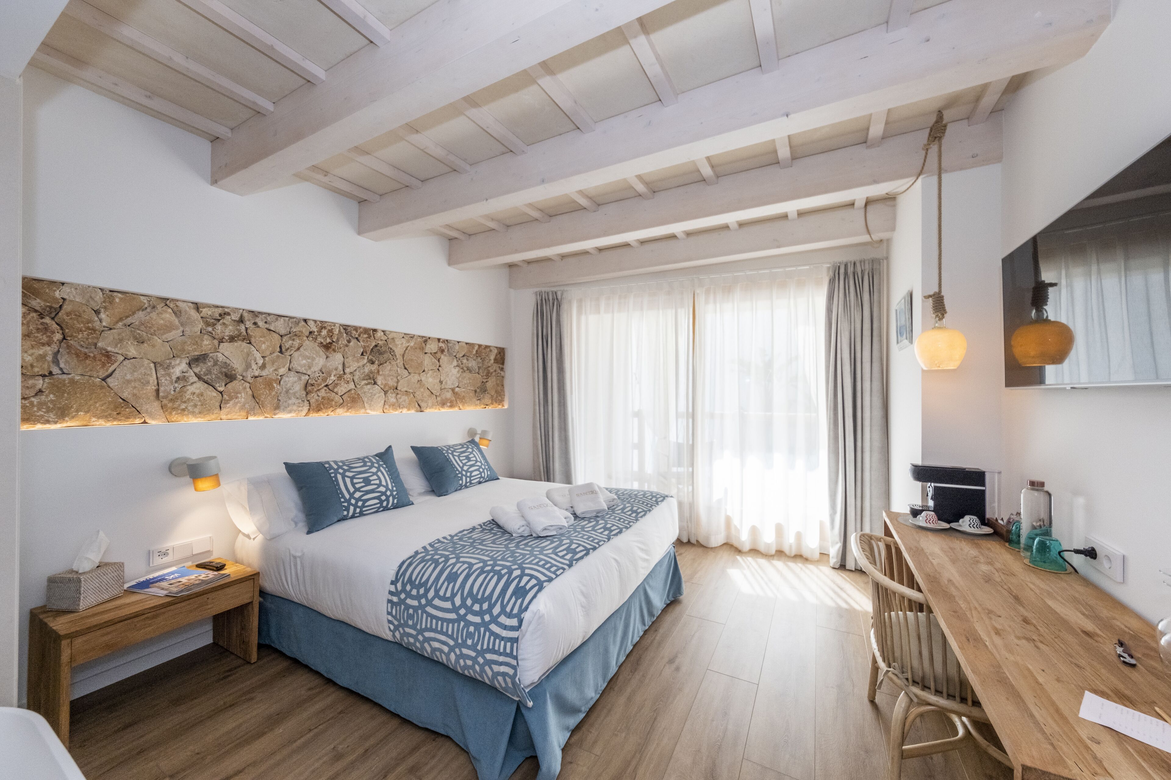 A bedroom with a bed, bedside table, lamp, and a stone wall.