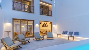 Un área de piscina moderna al aire libre con sillones de descanso y un comedor visibles a través de puertas de vidrio.