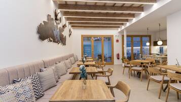 A modern dining area with wooden tables and chairs, a sofa with patterned cushions, and a large abstract wall art piece.