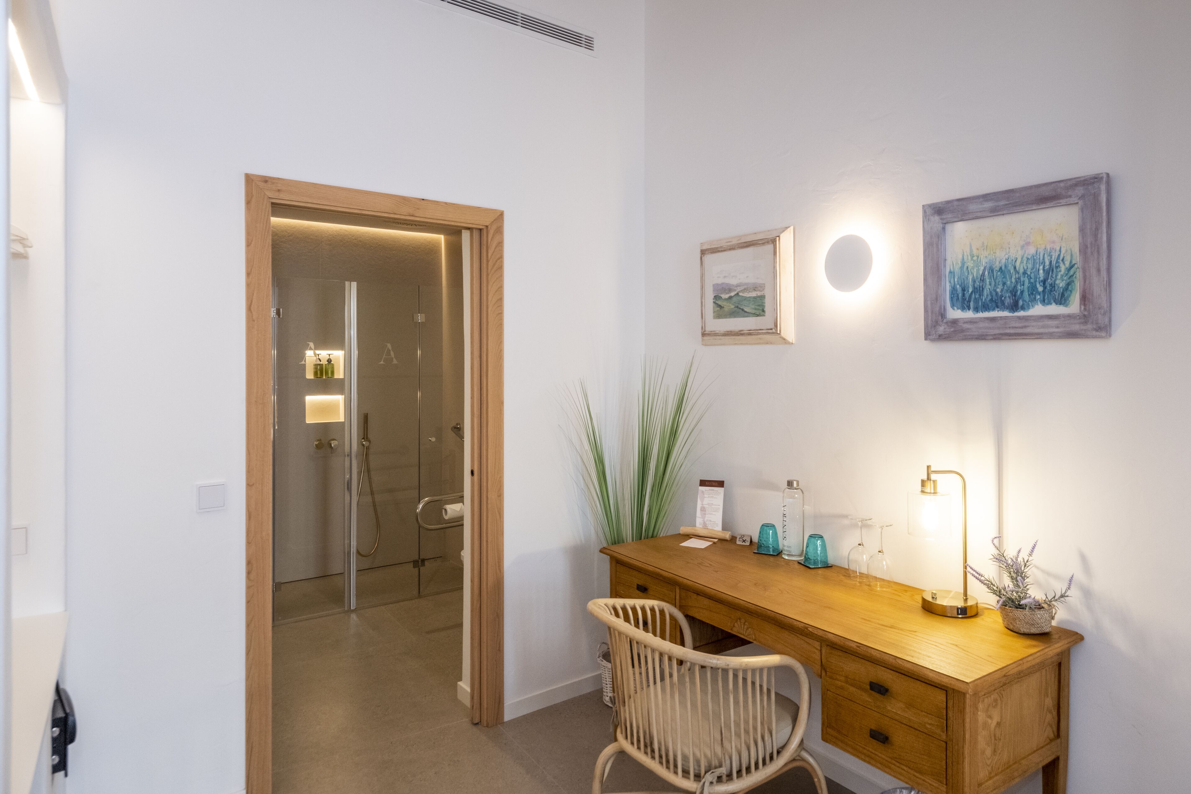 Un baño moderno con cabina de ducha de vidrio, un escritorio de madera con una silla y una lámpara de pared.