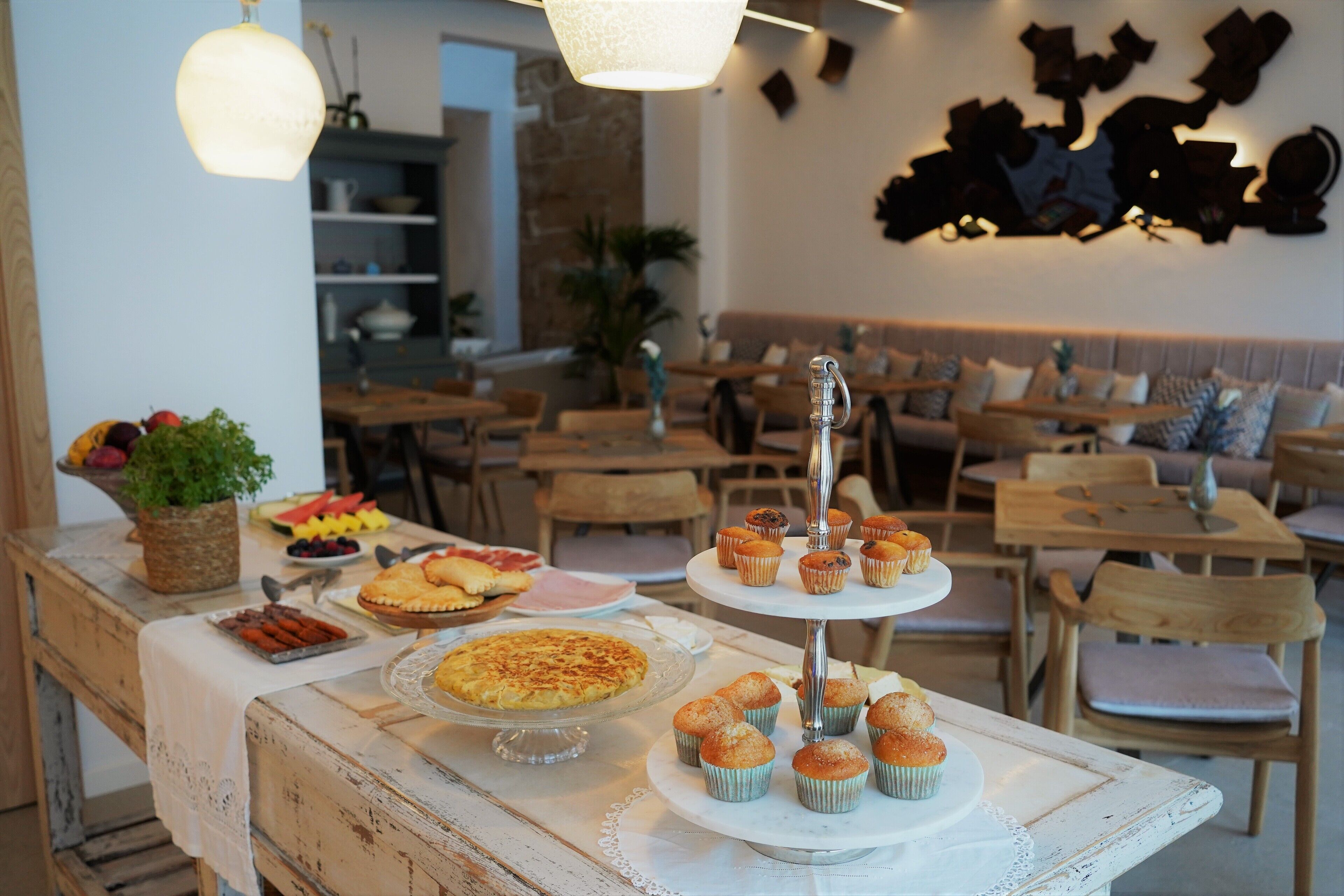 Un comedor con una mesa de buffet, un expositor de tres niveles con muffins, y una zona de estar con muebles de madera.