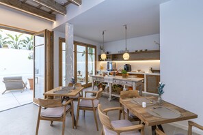 Una cocina moderna con armarios de madera, un comedor con mesas y sillas de madera, y un amplio ventanal con vistas a plantas.