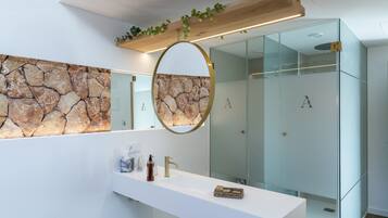 A modern bathroom with a stone wall backsplash, a large mirror, and a glass shower enclosure.