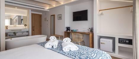 Une chambre d’hôtel comprenant un grand lit, un bureau, une chaise, une télévision, un coffre-fort et une salle de bain avec un miroir et un porte-serviettes.
