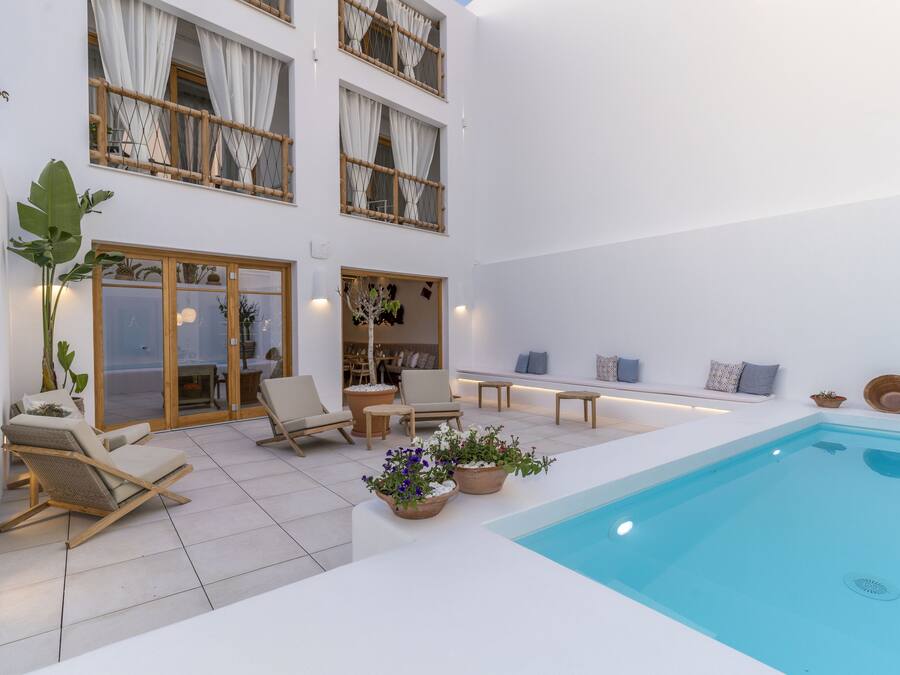 Un área de piscina moderna al aire libre con sillas de descanso, plantas en macetas y una zona de estar con cojines.