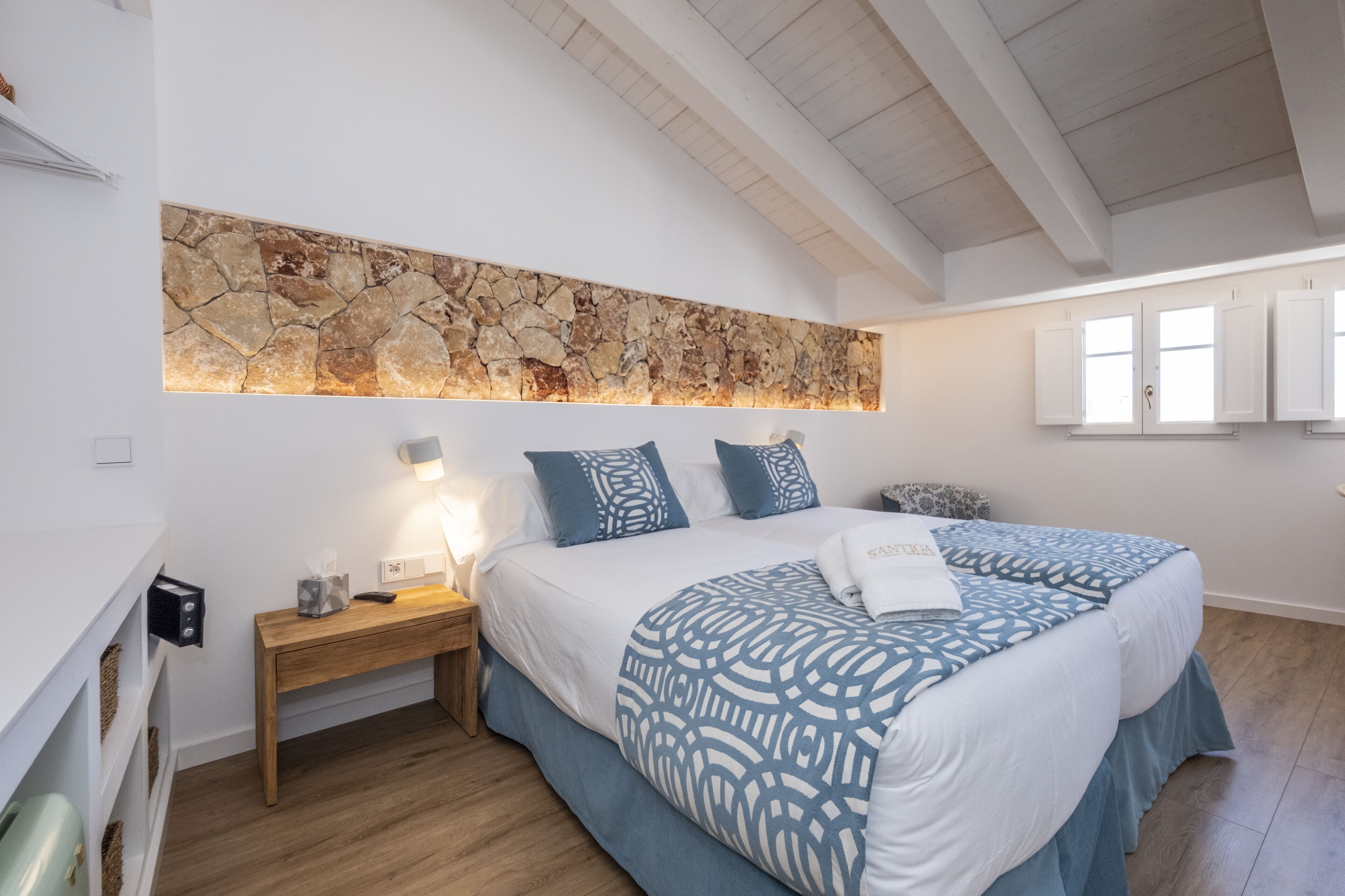 Una camera da letto con un letto grande, un comodino, un muro in pietra e un soffitto in legno.