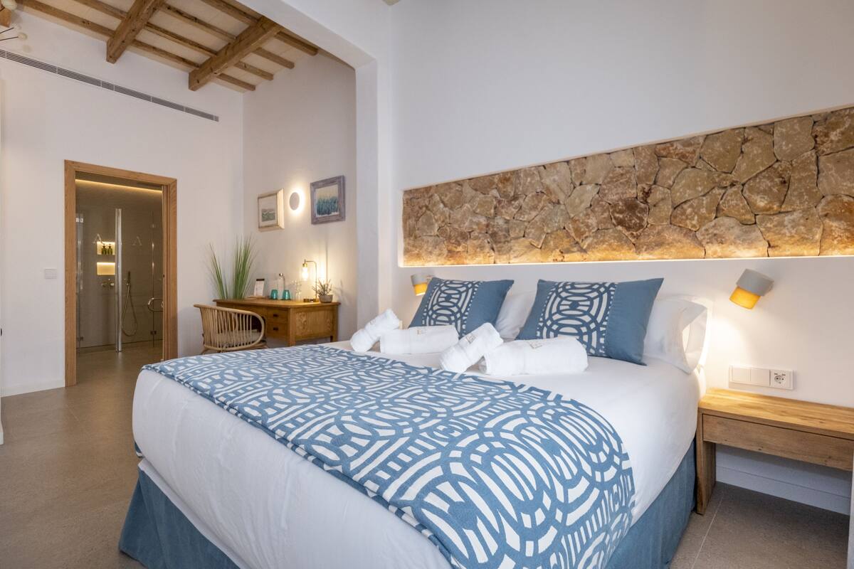 A modern bedroom with a large bed, a stone accent wall, and a wooden ceiling.