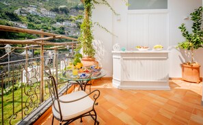 Un balcone con un tavolino in vetro, sedie e un vaso con una pianta.